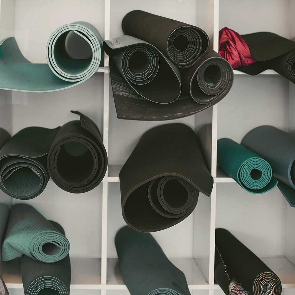 Schwarz-Weiss-Bild mit mehreren Pilates-Matten, teilweise gruen gefaerbt, in einem offenen Schrank.